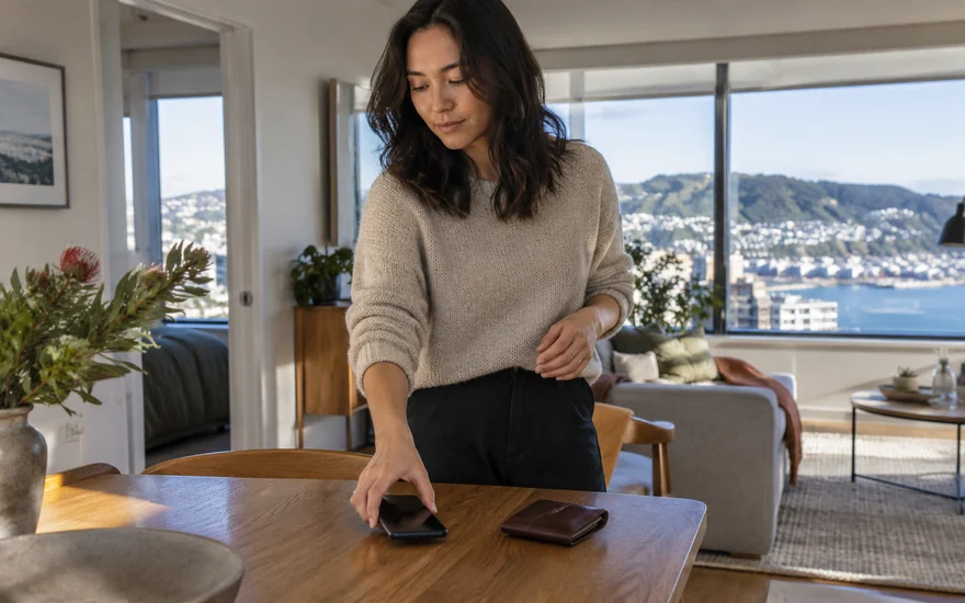 Neteller casino NZ: an adult arranging a phone and wallet beside a laptop in a New Zealand apartment